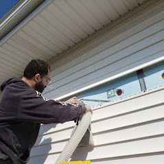 A man is using a vacuum hose to clean a window on a house.