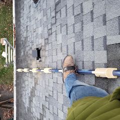 A person is standing on a roof with their feet on a pole.