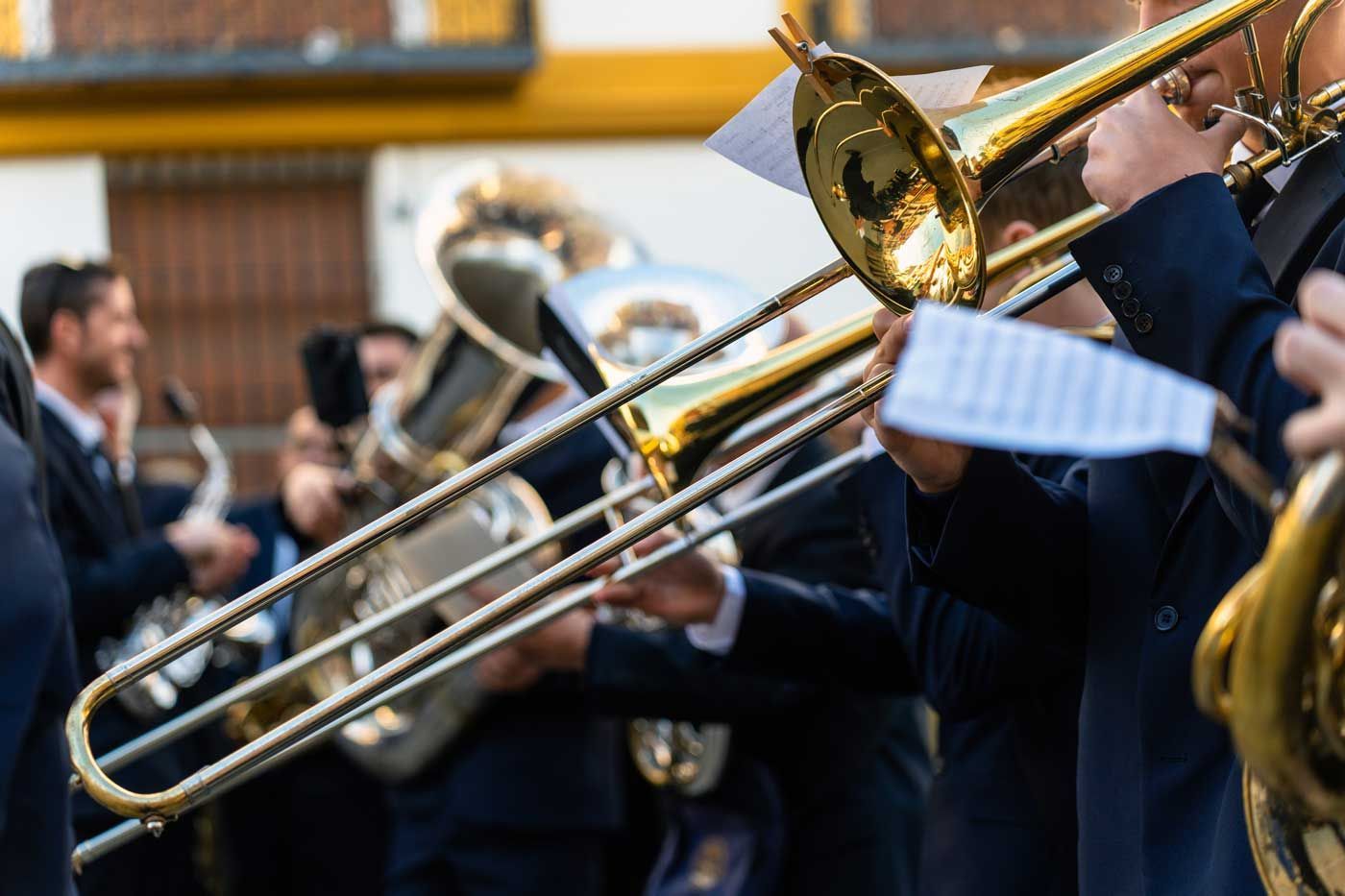 Brass band musicians playing trombones outdoors, wearing dark suits.