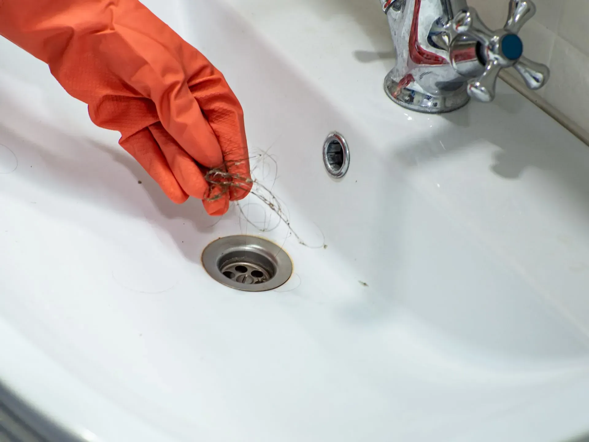 Person in orange glove removing hair from a bathroom sink drain.