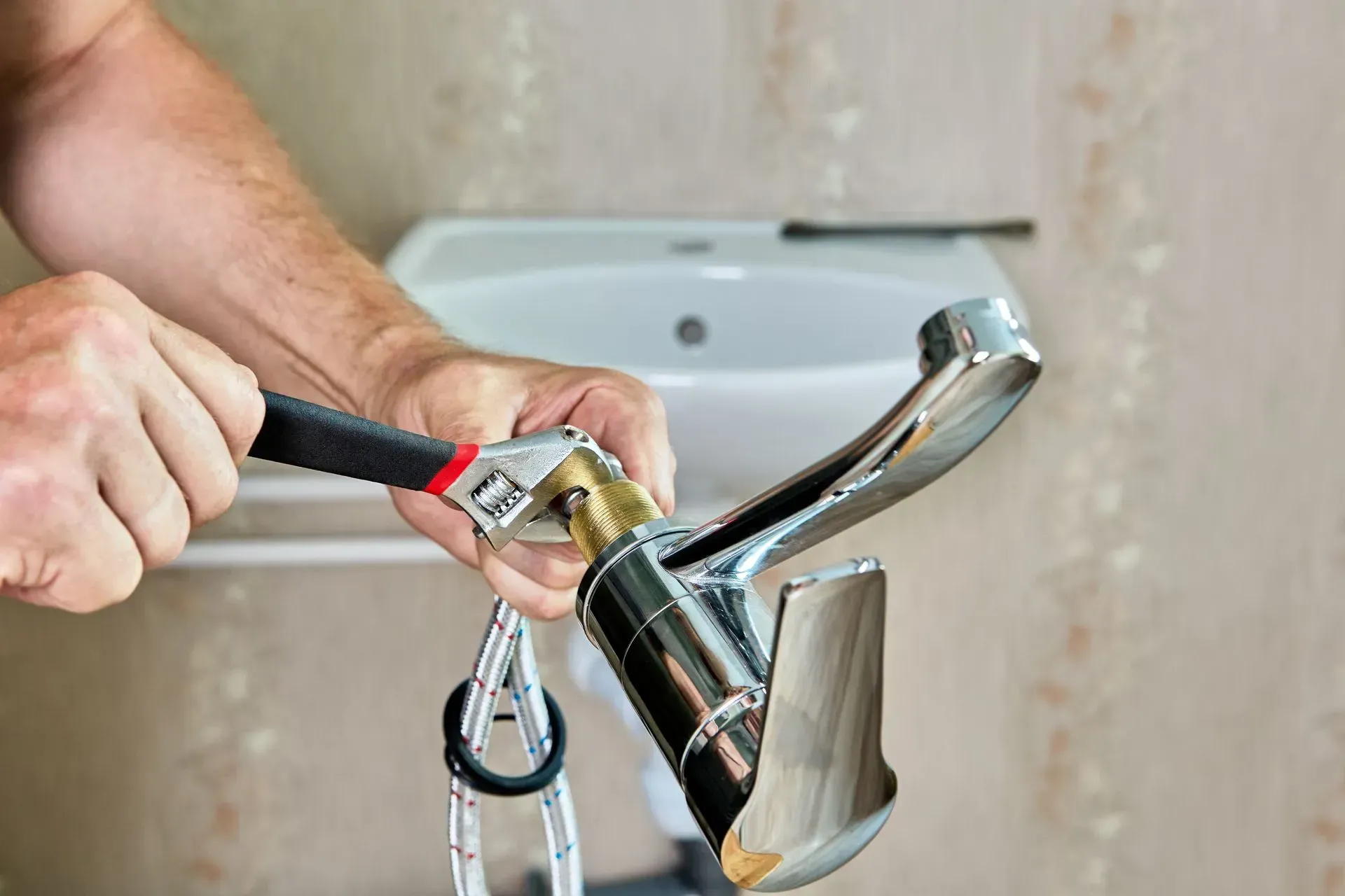 Person using a wrench to repair a chrome faucet in a bathroom.