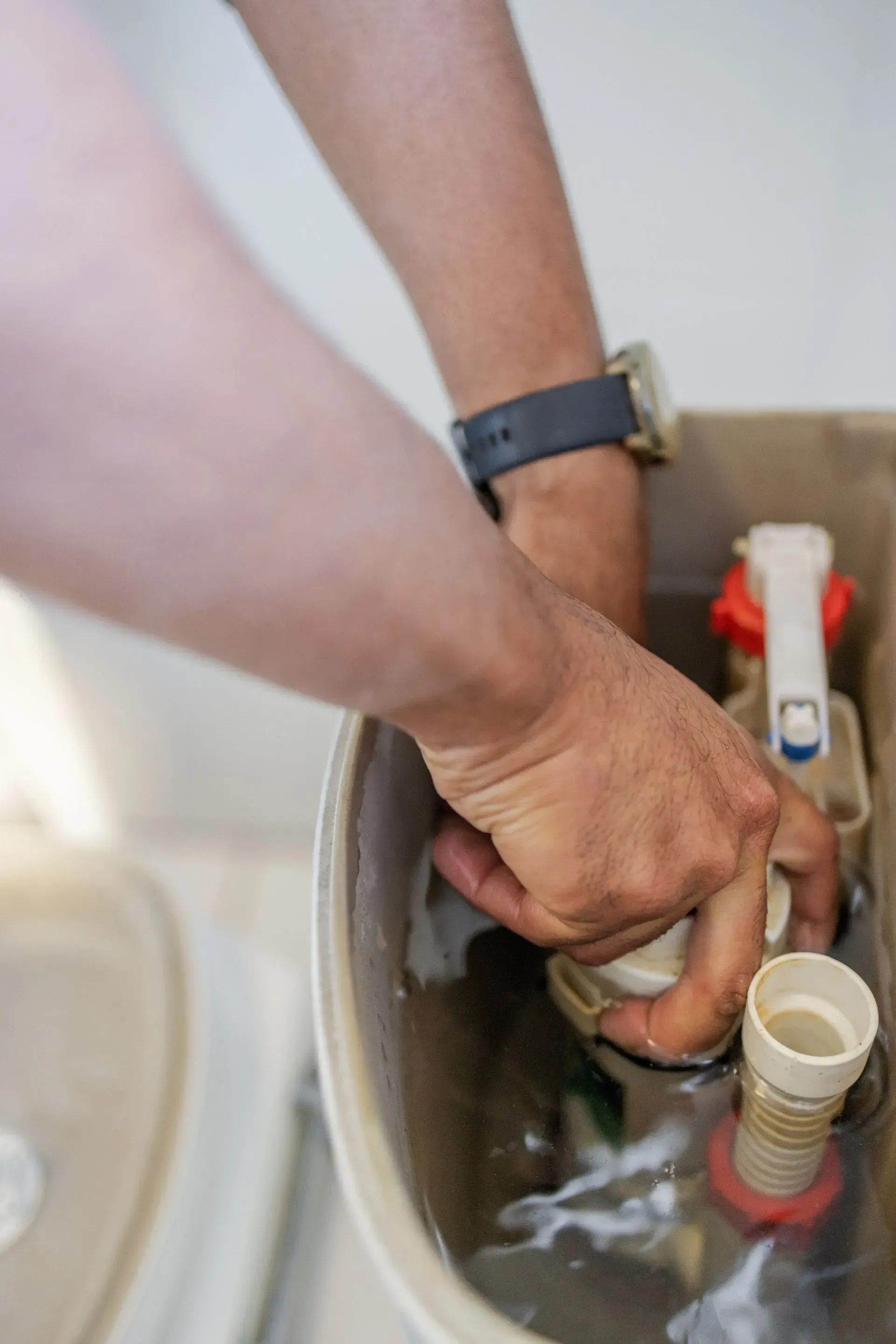Hands inside toilet tank, adjusting plumbing parts.