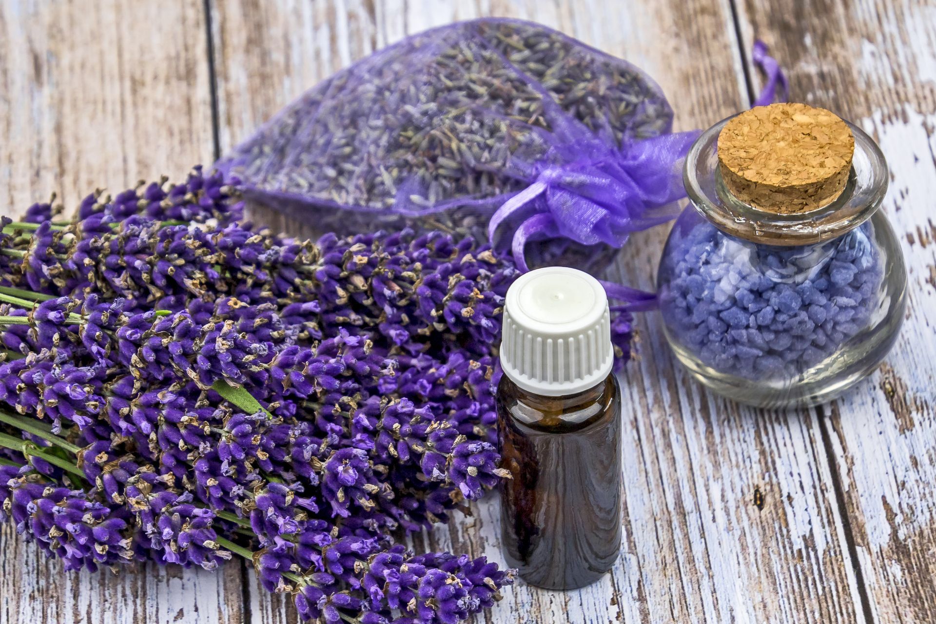 Un bouquet de fleurs de lavande, une bouteille d'huile essentielle et un sachet de lavande sur une table en bois.
