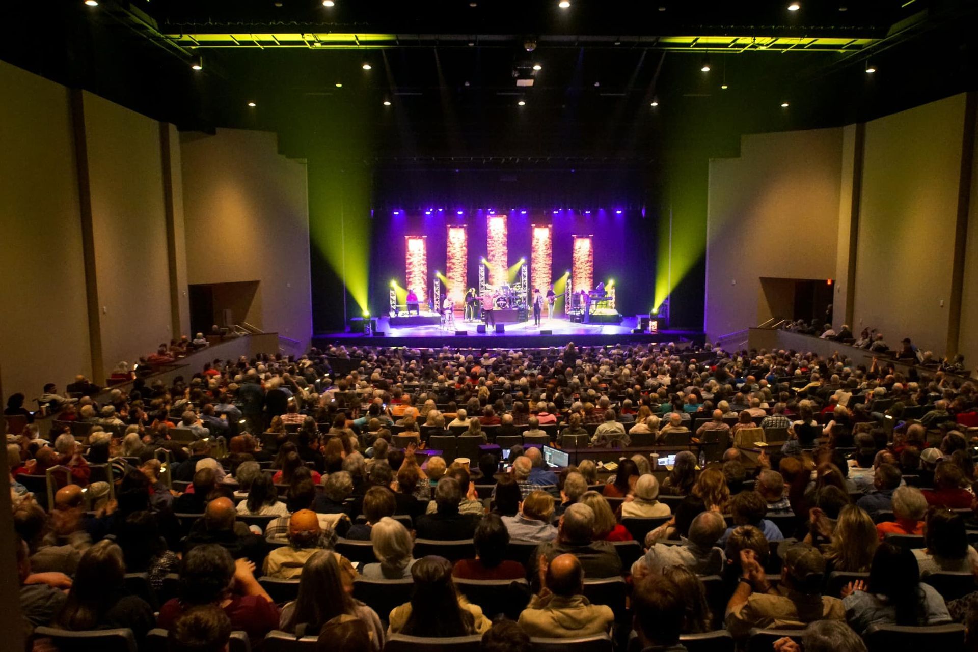 Audience watches band performing on a stage with lights in a large theater.