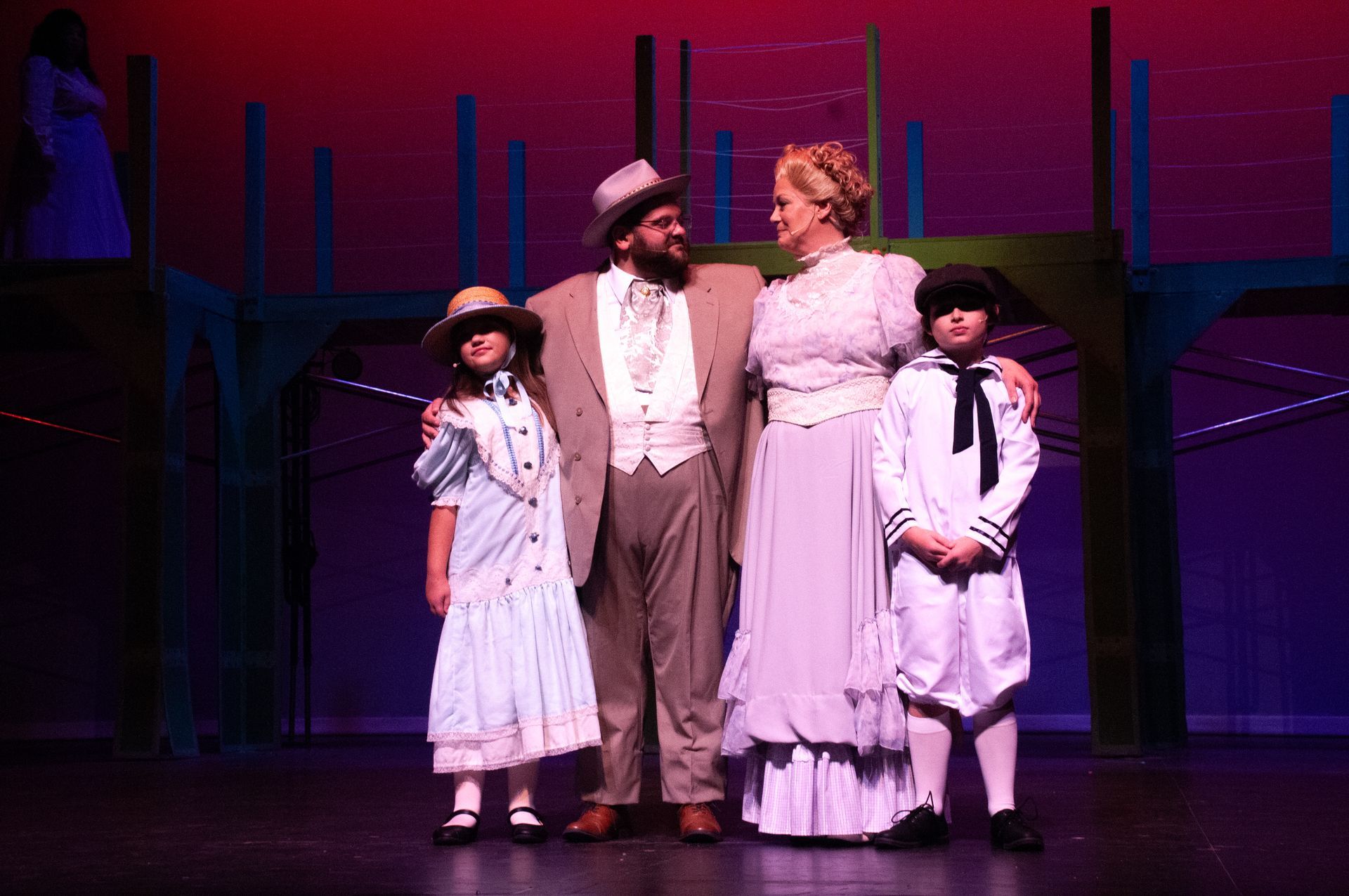 A family of four on stage, dressed in Victorian clothing, smiling.