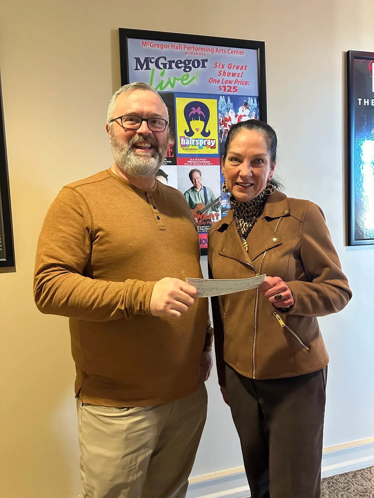 Two people holding a check in front of a poster; man with beard smiles, woman smiles.