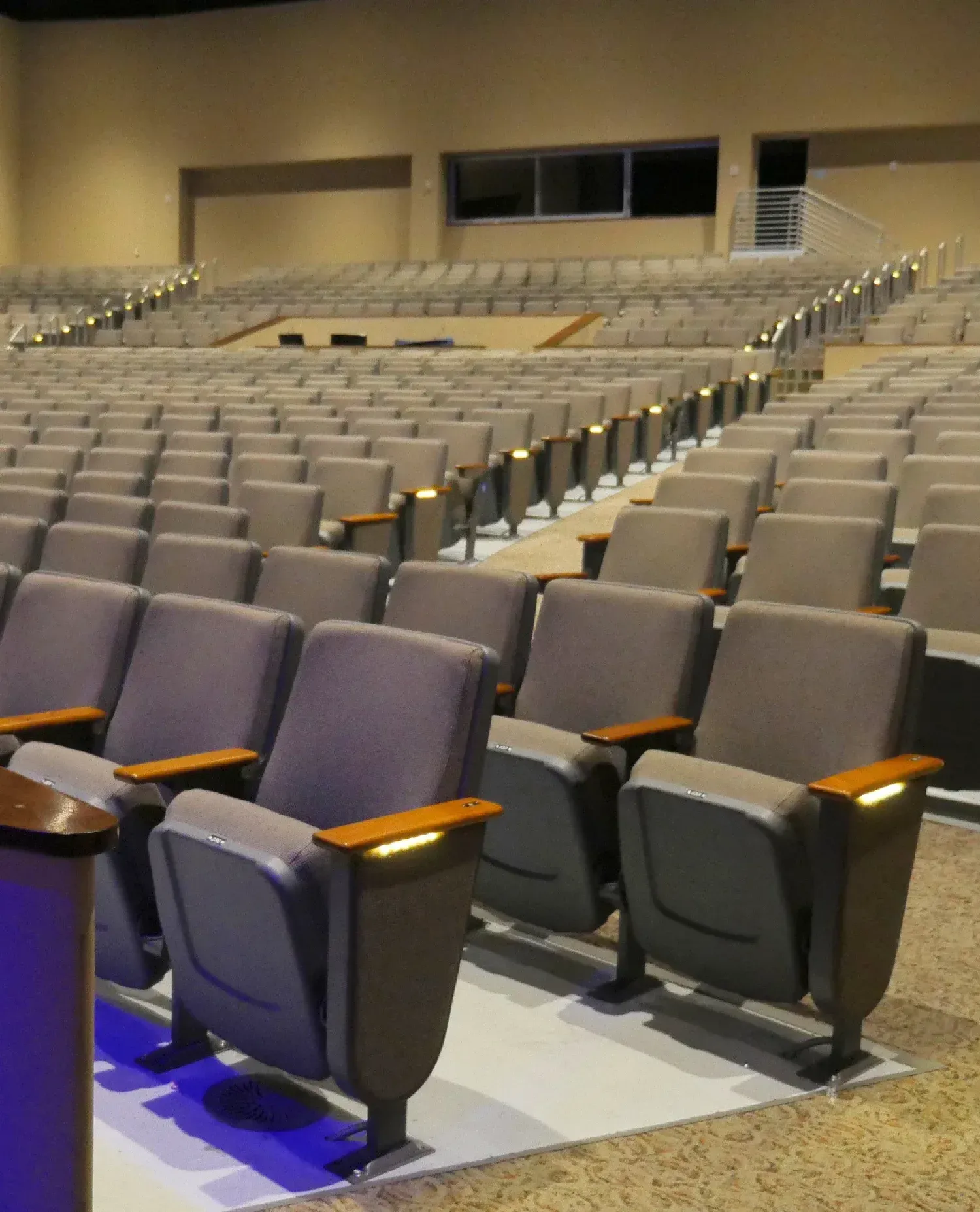Rows of gray theater seats in an auditorium with wood armrests and ambient lighting.