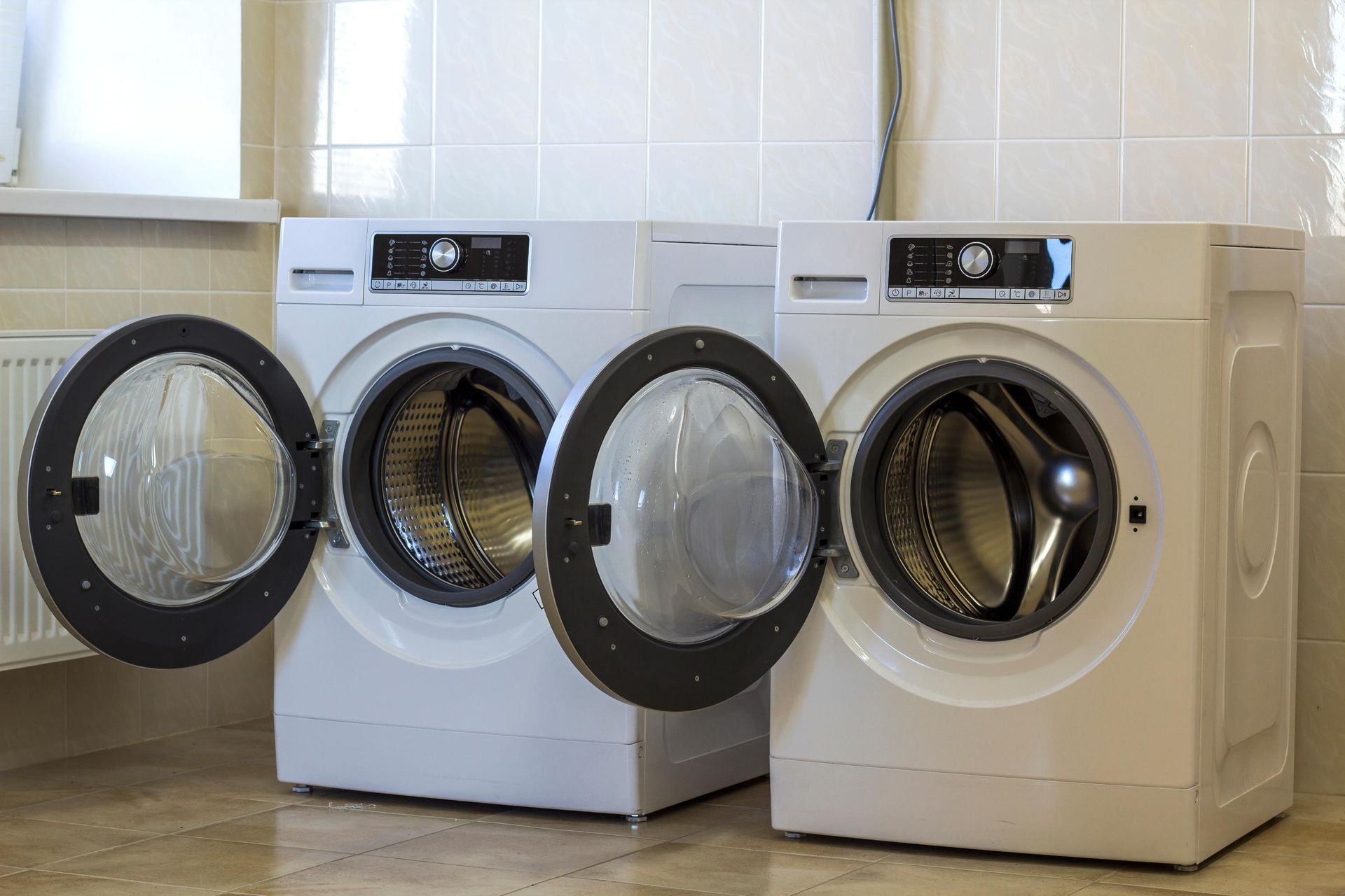 Two white washing machines with open doors in a tiled room.