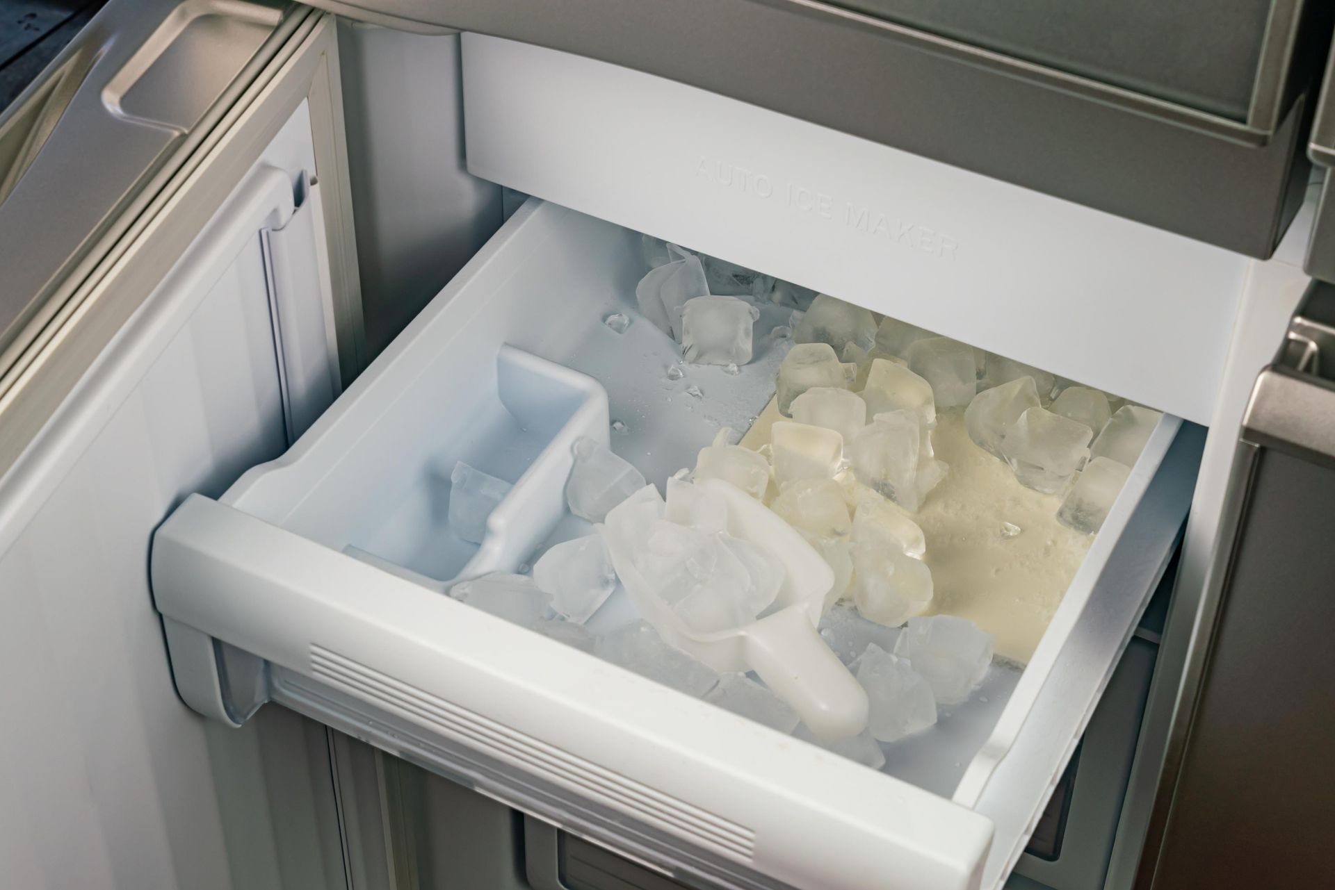 Open refrigerator ice drawer filled with ice cubes and scoop.