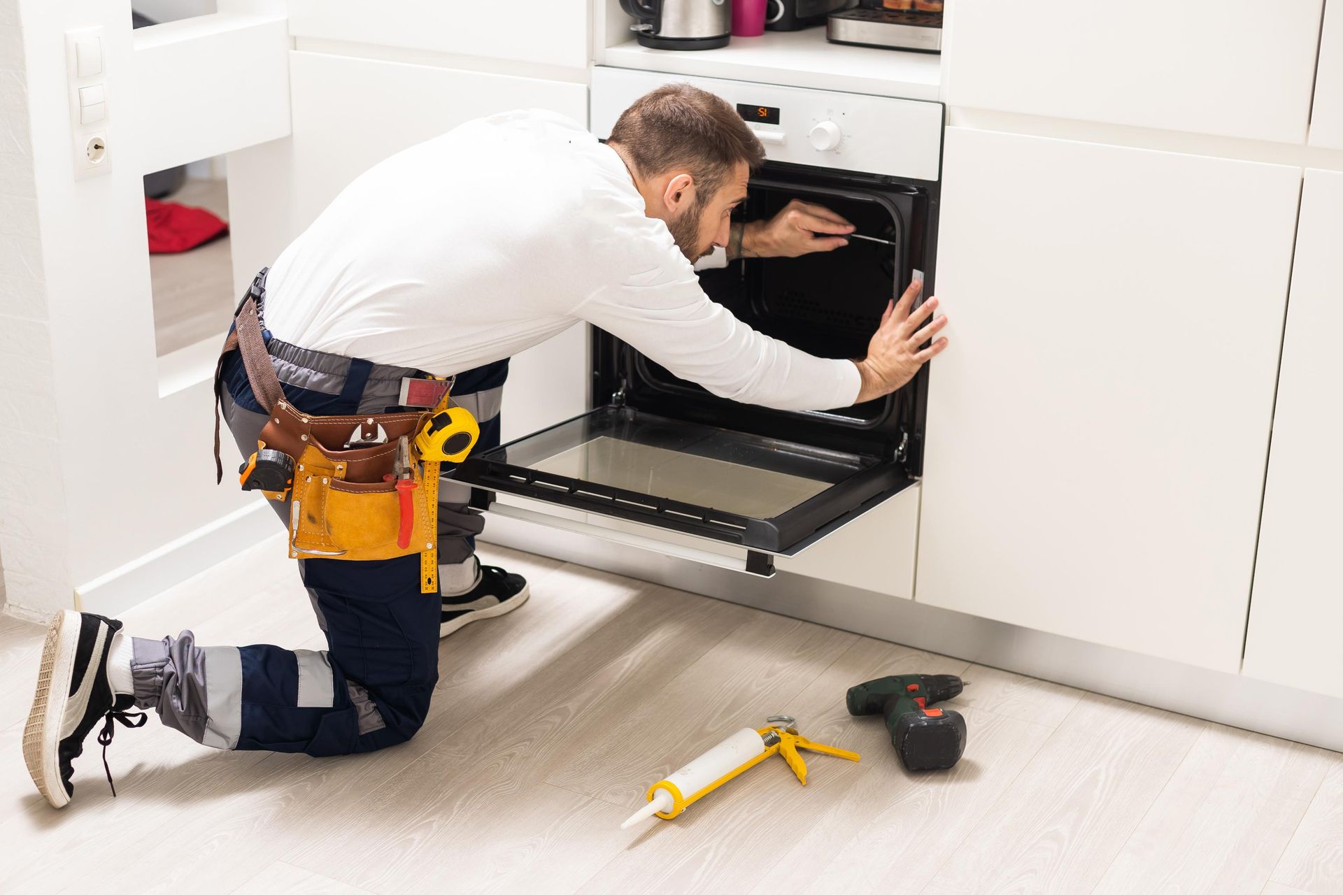 A repairman kneels to fix an oven, tools nearby.