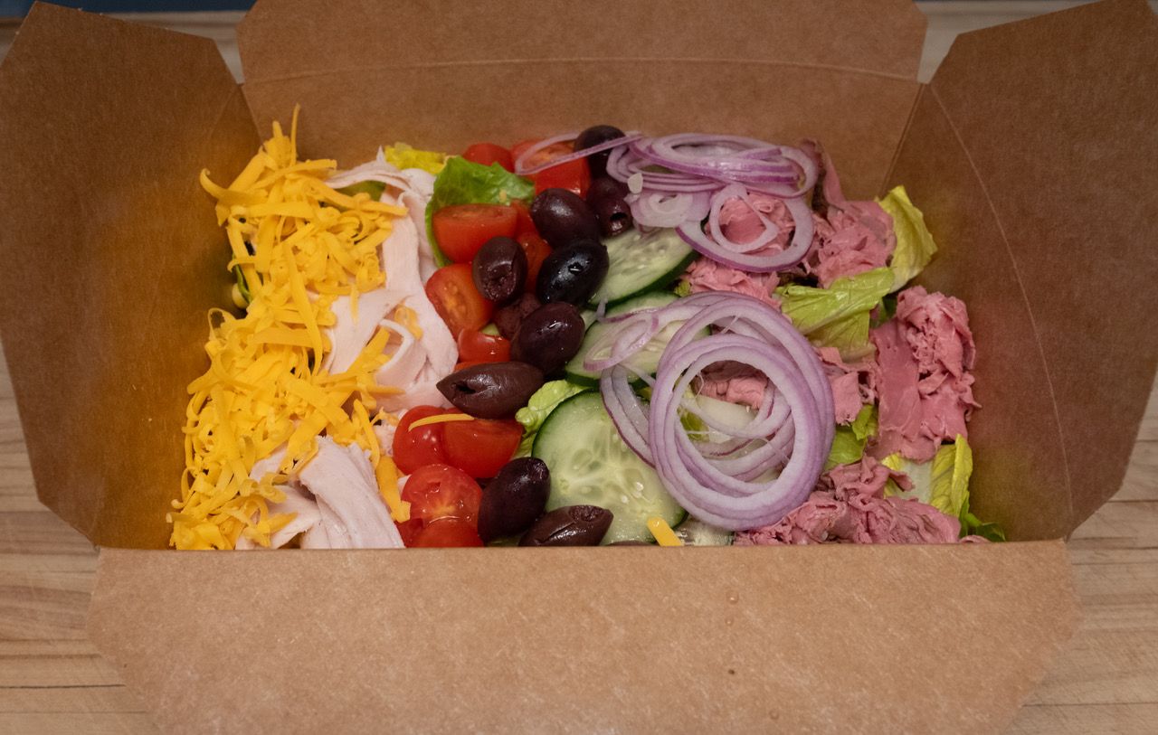 A salad in a cardboard box on a wooden table.