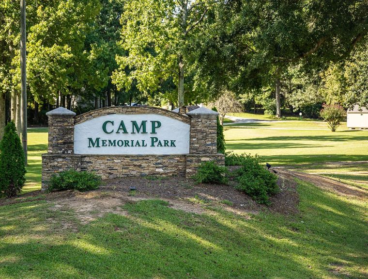 A sign for camp memorial park is sitting in the middle of a grassy field.