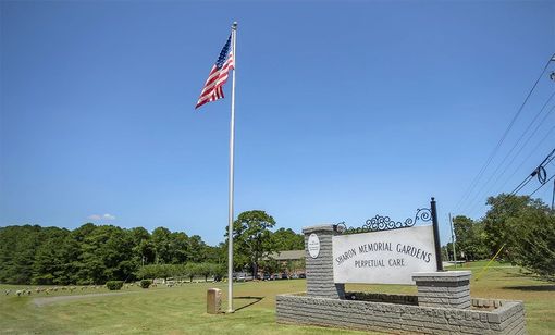 An american flag is flying in front of a sign for a cemetery.