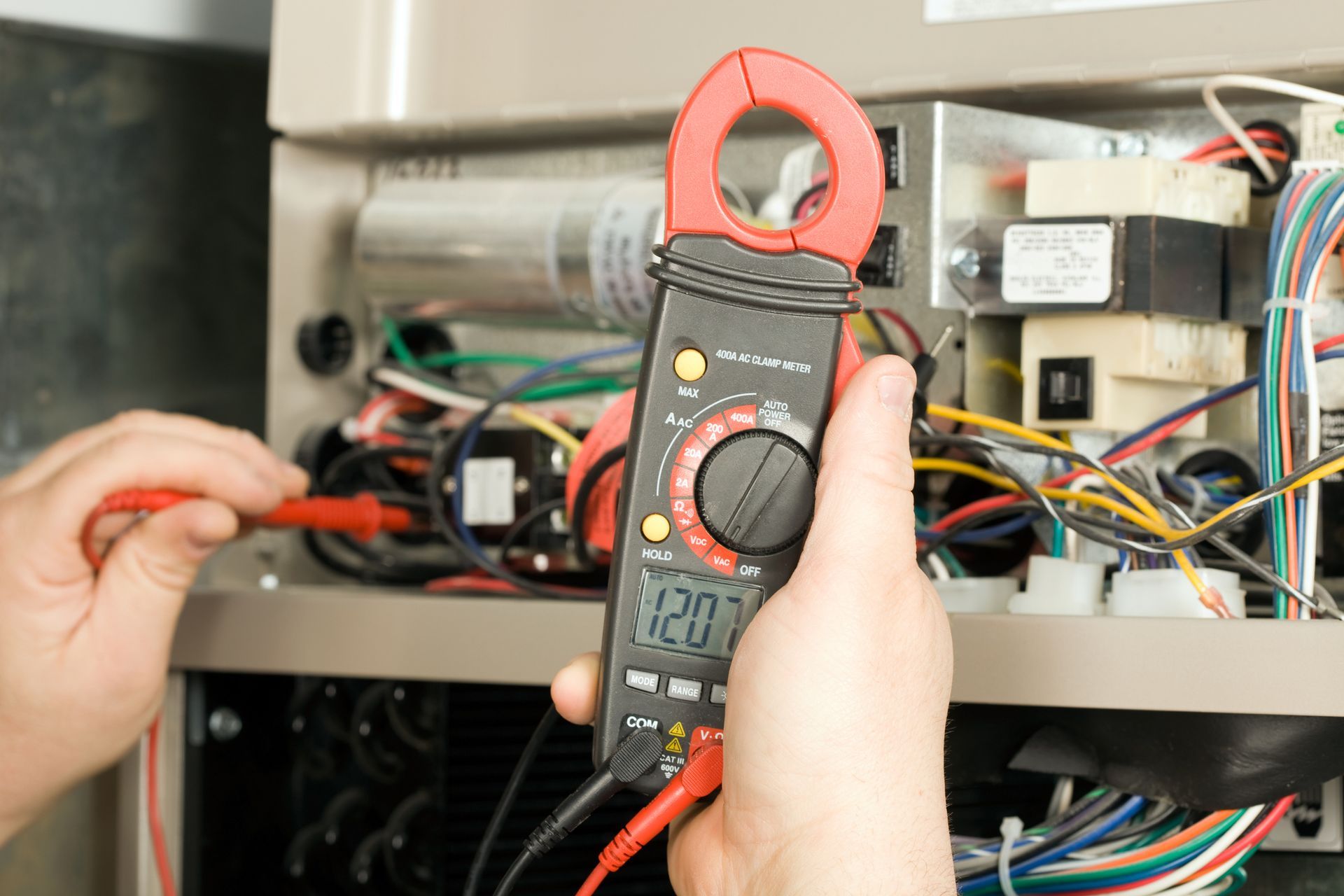A person is holding a clamp meter in front of a heater.
