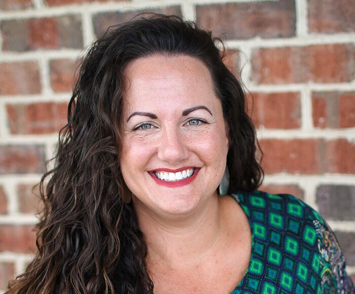 A woman is smiling in front of a brick wall.