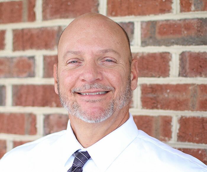A man in a white shirt and tie is smiling in front of a brick wall.