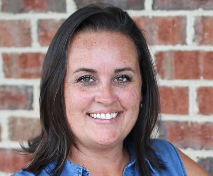 A woman is smiling in front of a brick wall.
