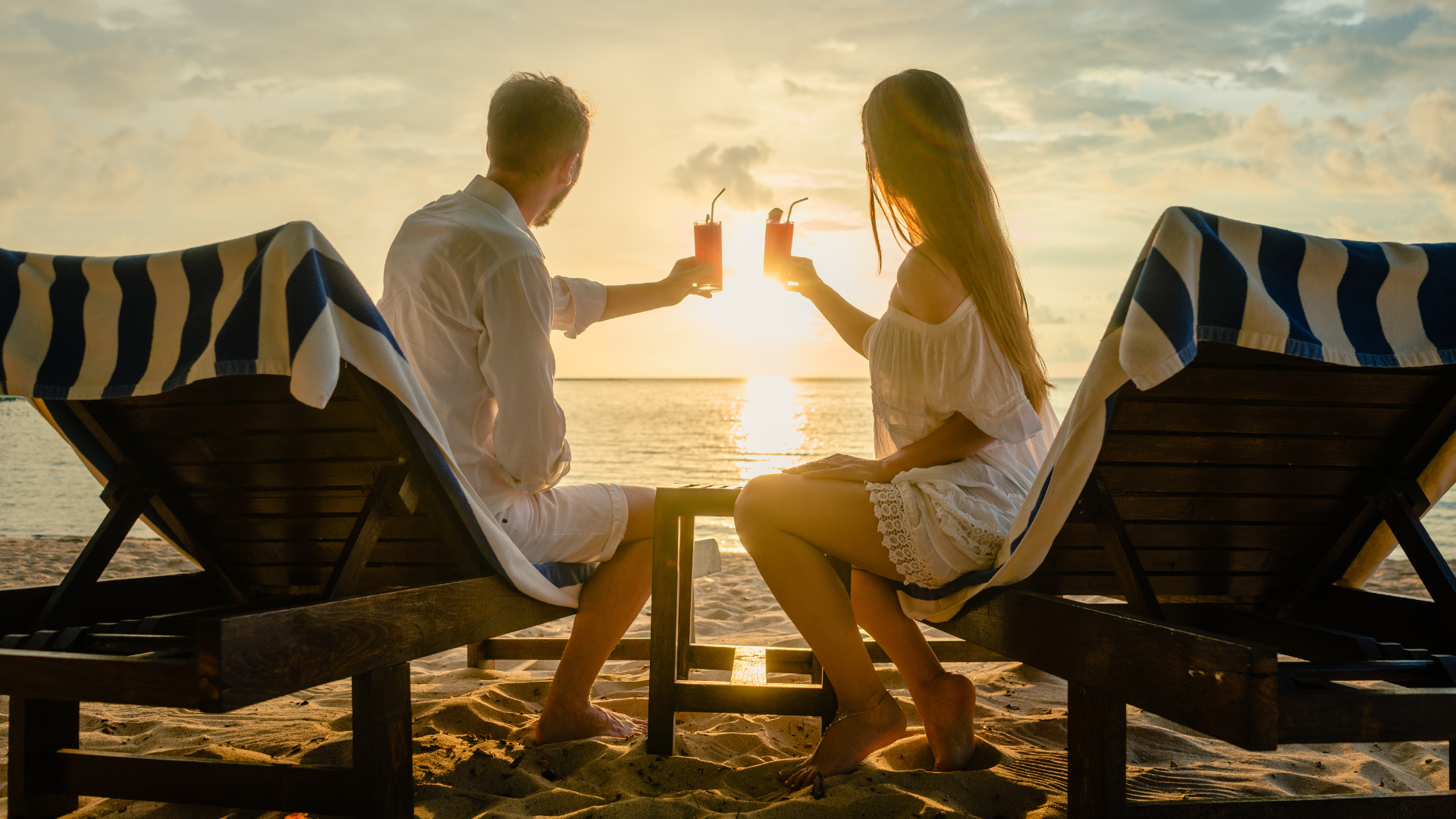 Couple toasting cocktails on beach at sunset.