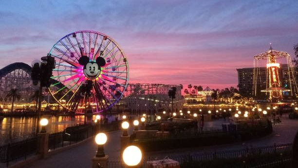 Ferris wheel with Mickey Mouse lights, reflecting on water at dusk, Disneyland park.