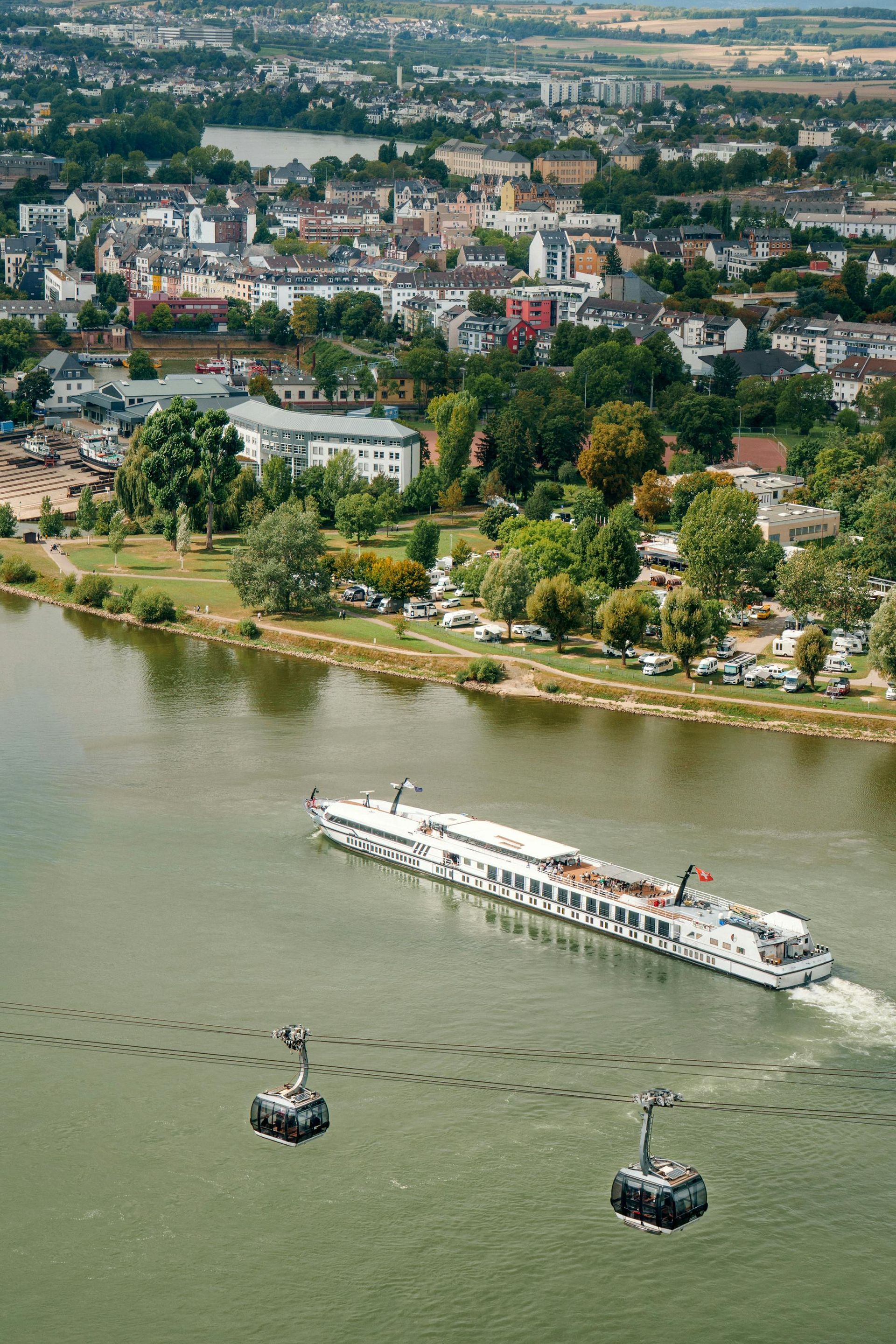 River cruise ship and cable car over a river with a city in the background.