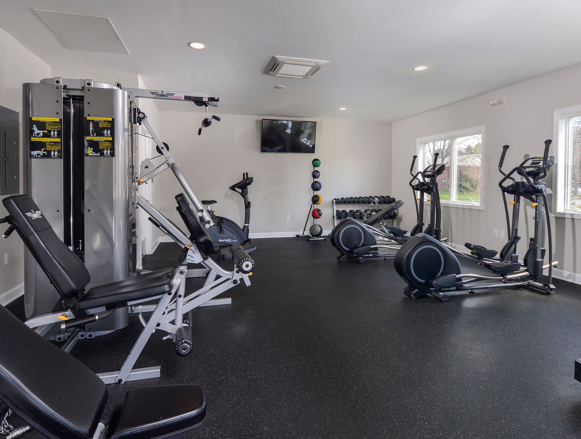 Indoor fitness center with treadmills, elliptical machines, weights, and a wall-mounted TV.