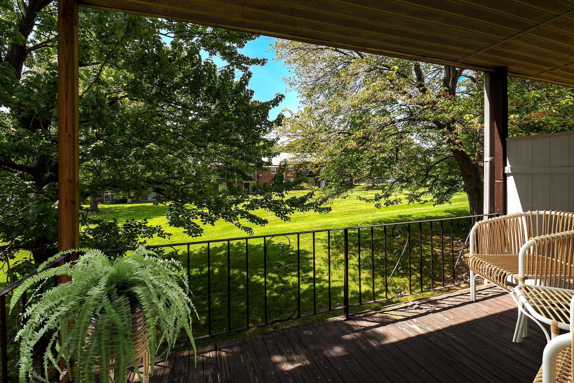 Balcony with wicker chairs overlooks a grassy, tree-filled courtyard.