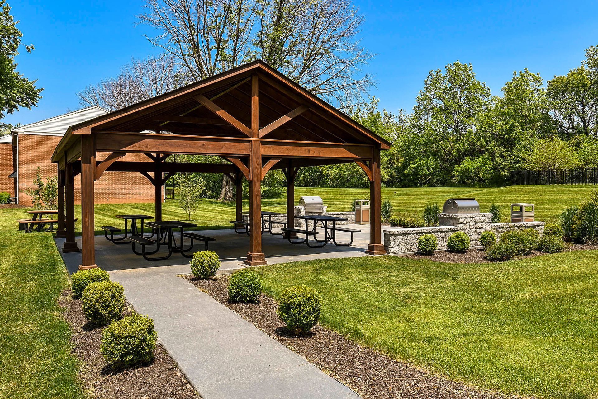 Wooden pavilion with picnic tables and grills in a grassy park.