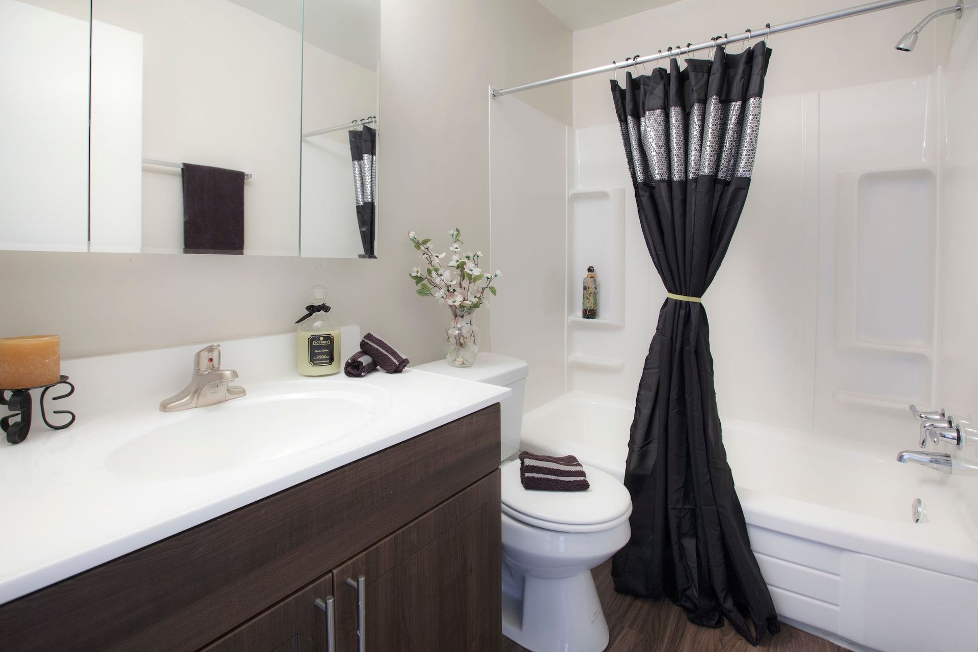 Bathroom with a white countertop sink, dark wood vanity, toilet, and a tub/shower with a black-gray curtain.