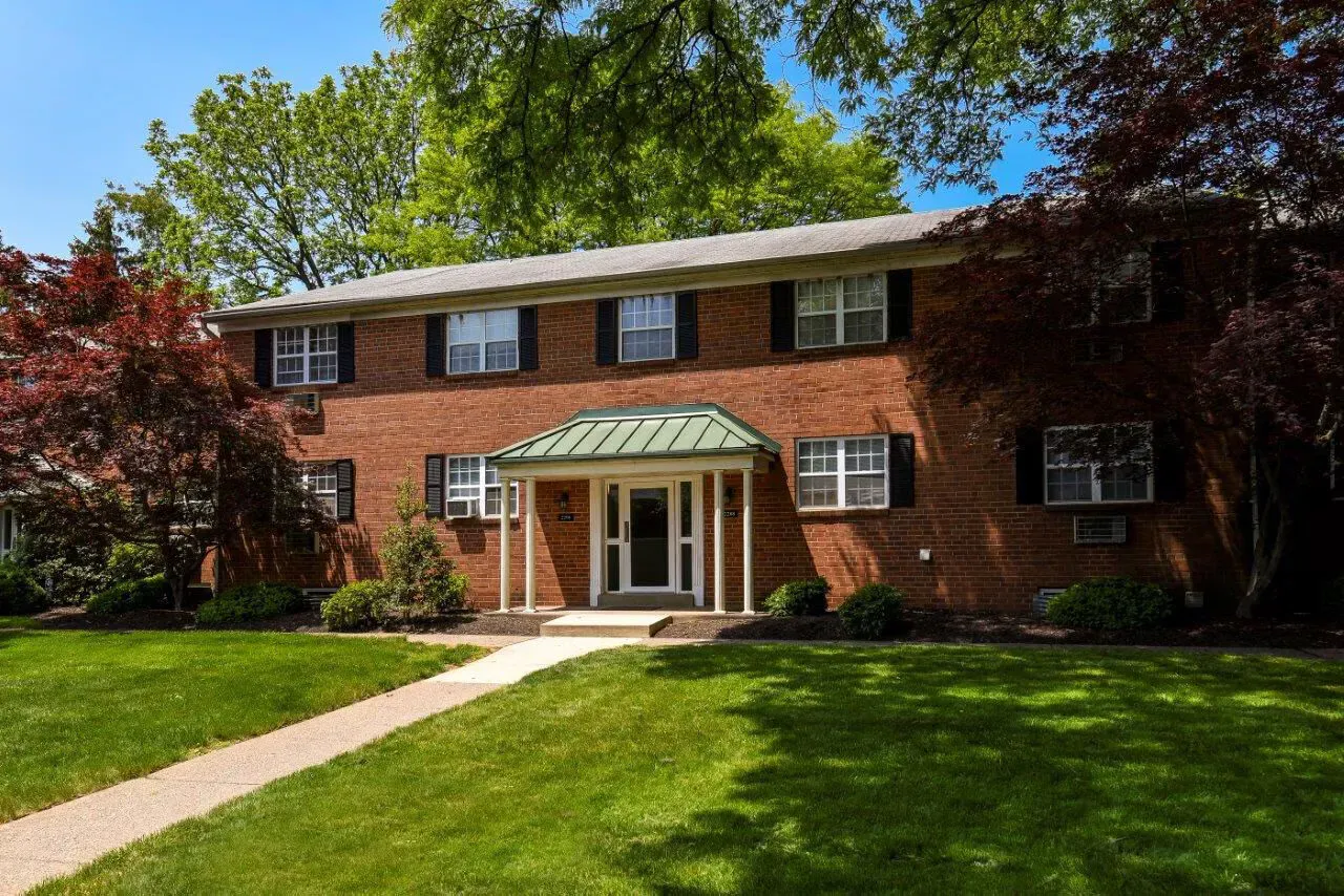 Two-story brick apartment building with a green lawn and trees.
