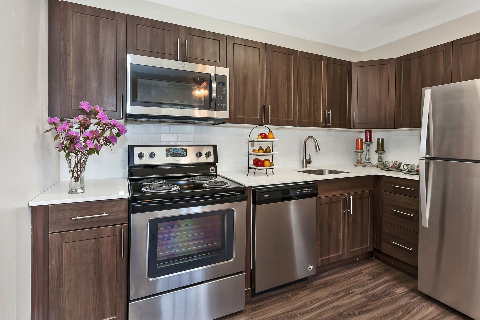 Modern kitchen with dark wood cabinets, stainless steel appliances, and white countertops.