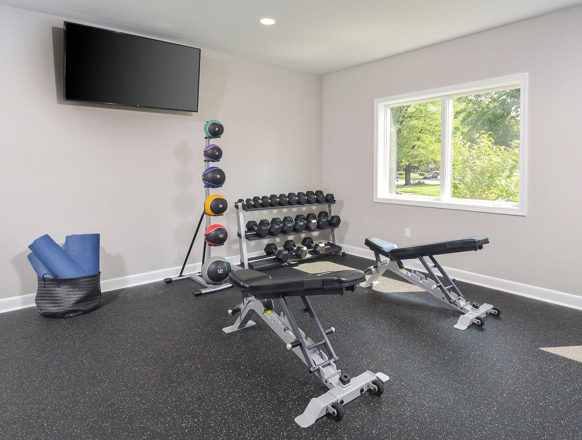 Well-lit community fitness room with free weights, benches, and a wall-mounted TV.