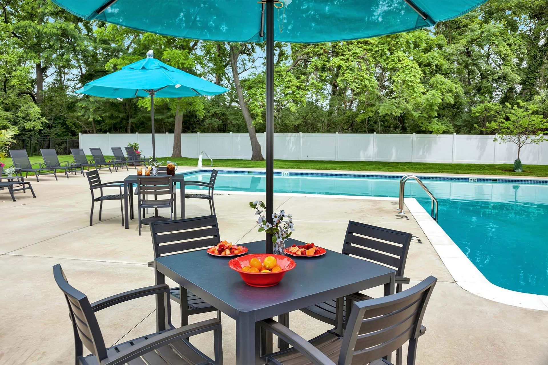 Outdoor apartment community pool area with seating and blue umbrellas.