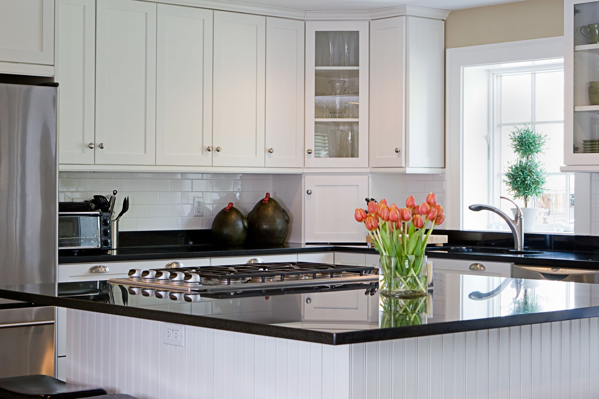 Bright white kitchen with black countertops, a gas stove, and a vase of pink tulips on the island.
