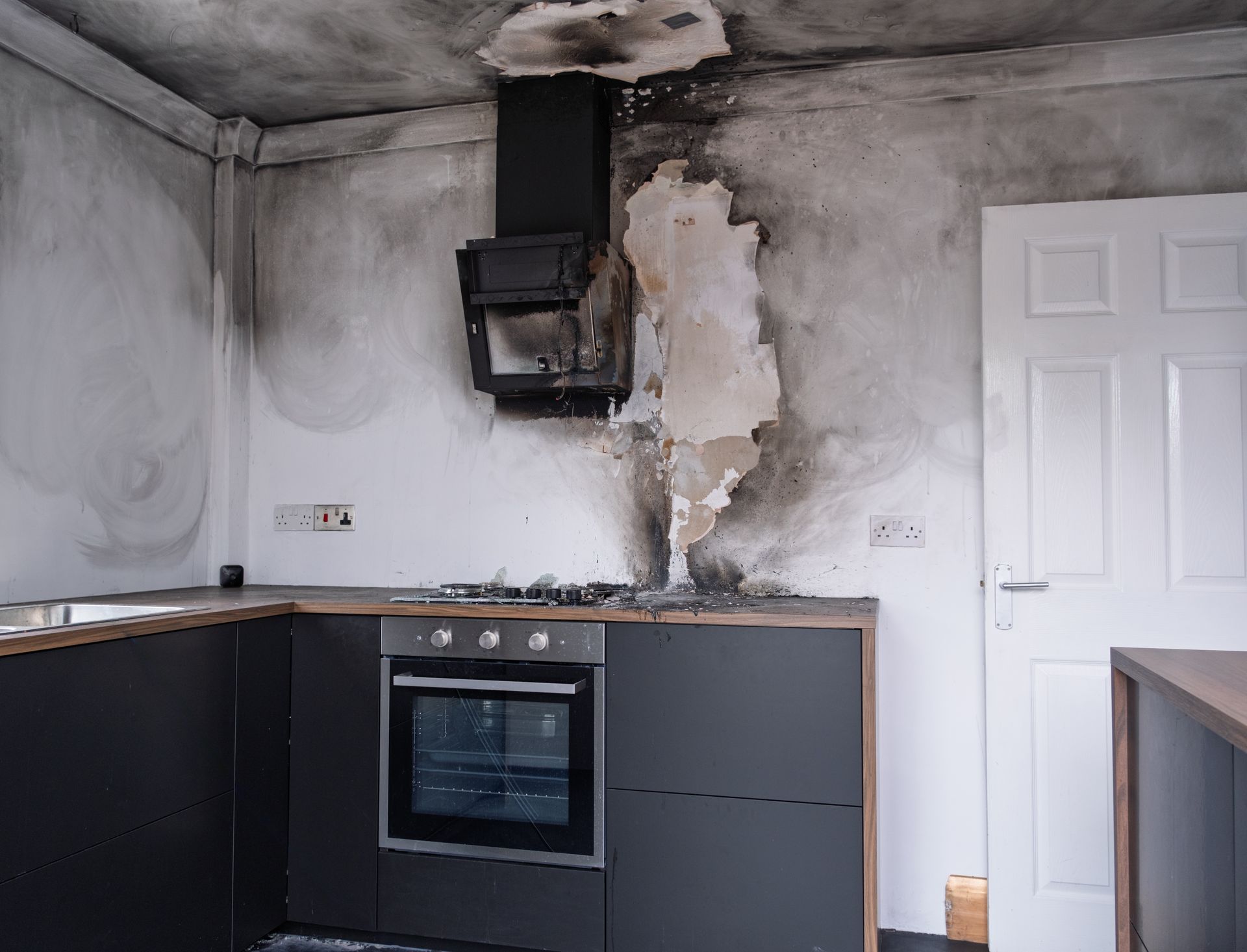 Damaged kitchen wall and ceiling around a black extractor fan, with smoke stains and peeling plaster