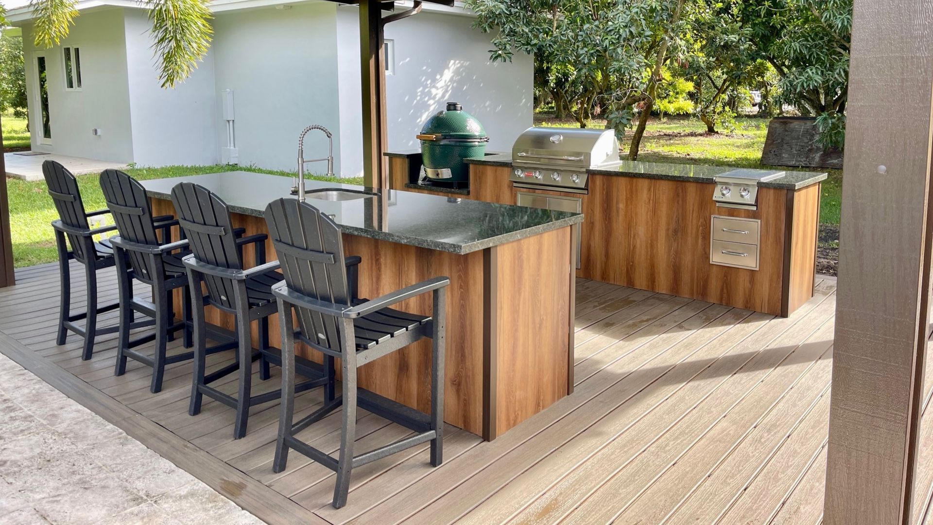 Outdoor kitchen island with granite countertop and black bar stools on a wooden deck