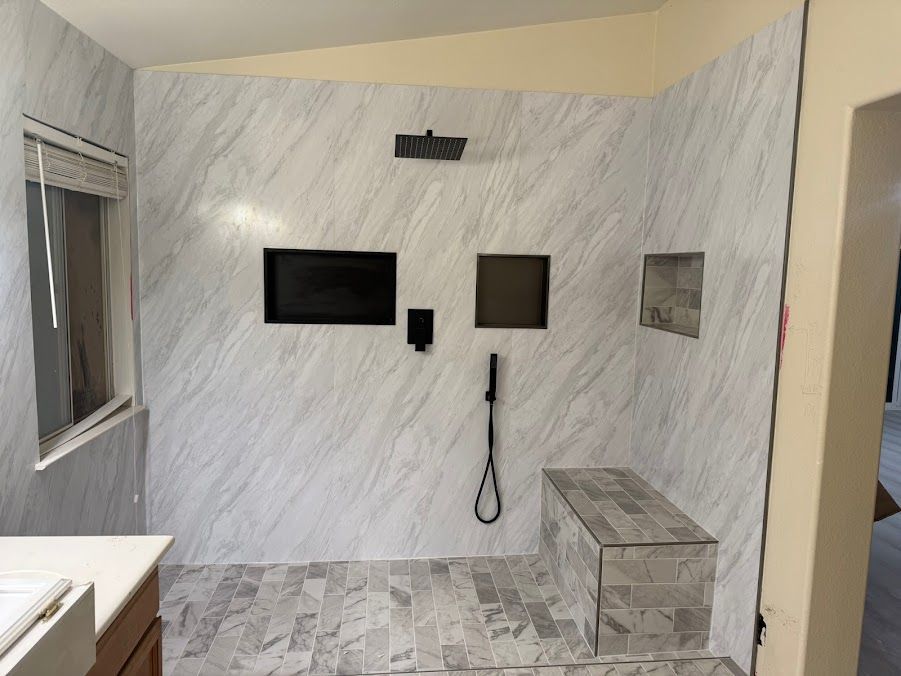 Modern tiled bathroom with wall-mounted TV, mirror, phone, and bench in a shower area