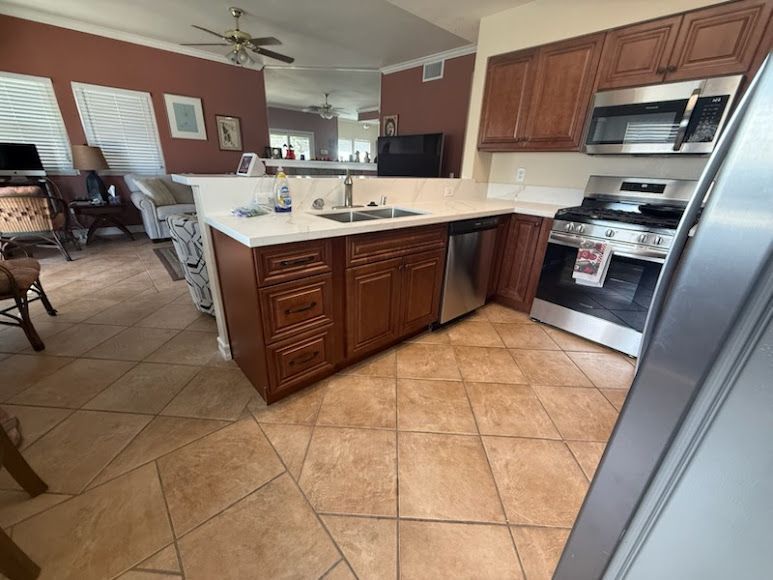 Kitchen with tile floor, wood cabinets, island counter, and stainless steel appliances.