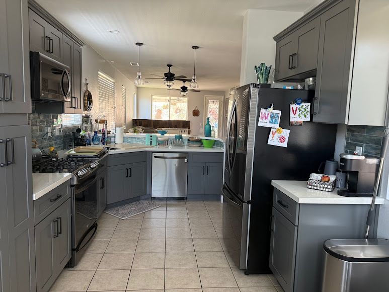Modern kitchen with gray cabinets, black appliances, and a central island, lit by pendant lights.