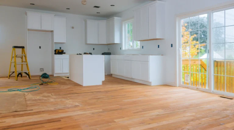 Bright unfinished kitchen with white cabinets, wood floors, and sliding glass doors opening to a deck.