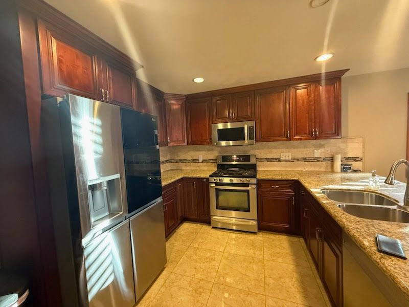 Modern kitchen with stainless steel appliances, dark wood cabinets, and tan tile flooring