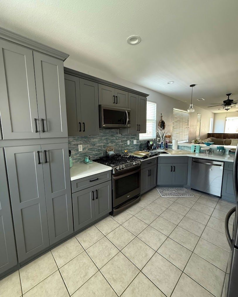 Modern gray kitchen with tiled floor, black appliances, and light countertops open to a dining area