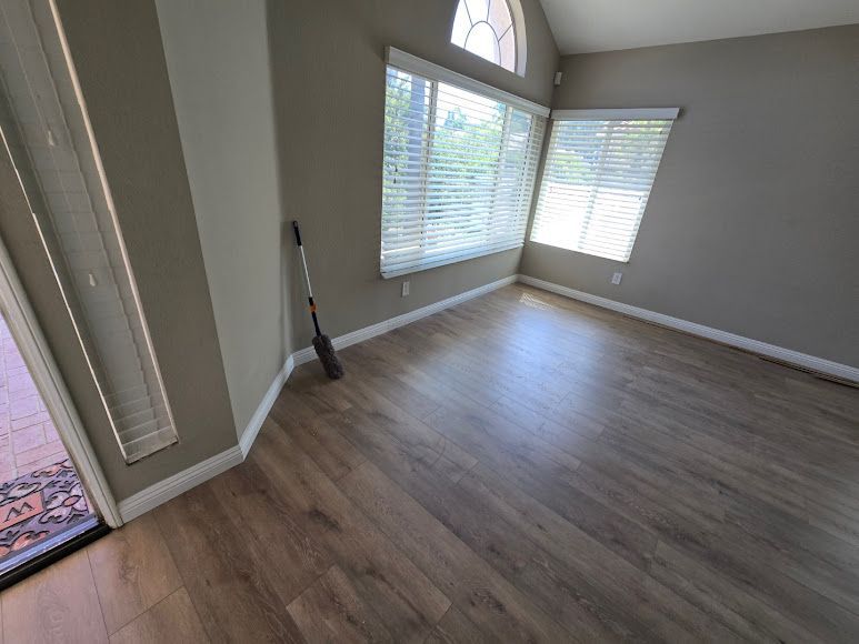 Empty gray room with wood-look floor, large windows, and a broom by the wall.