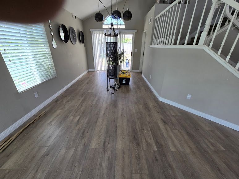 Empty living room with gray wood floors, wall decor, staircase, and front door