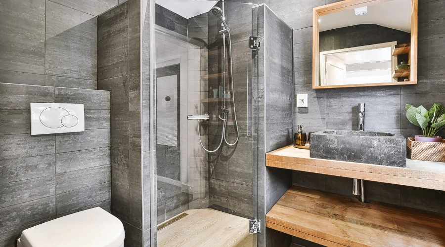 Modern gray-tiled bathroom with glass shower, toilet, floating wood vanity, and mirror cabinet