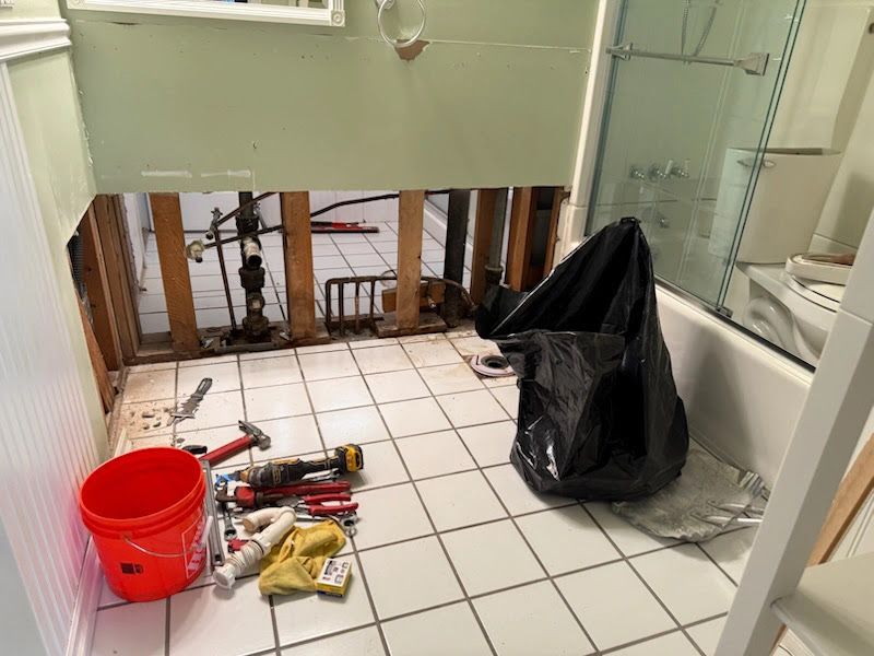 Bathroom under renovation with exposed wall studs, tools on the tile floor, and a black trash bag.