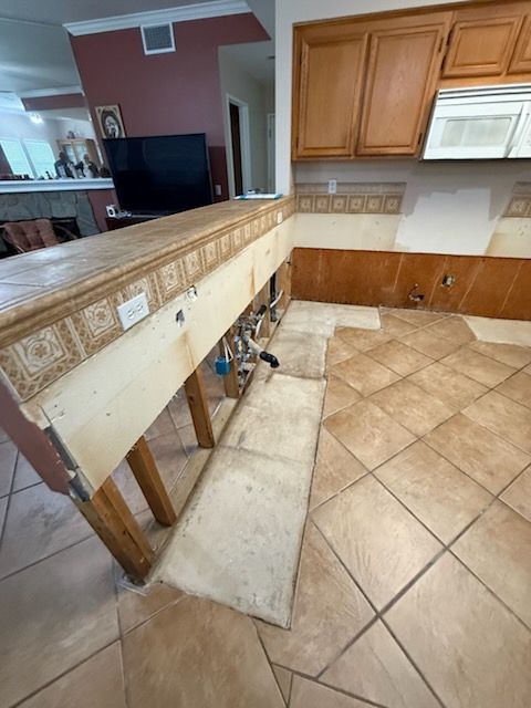 Kitchen renovation with exposed cabinet framing, tan tile floor, and granite countertop peninsula