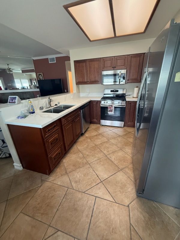 Modern kitchen with brown cabinets, granite island, stainless appliances, and tan tile floor