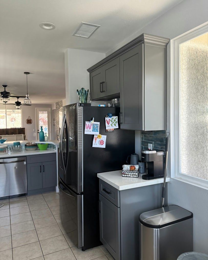 Modern kitchen with black refrigerator, gray cabinets, and a coffee maker beside a stainless trash can.