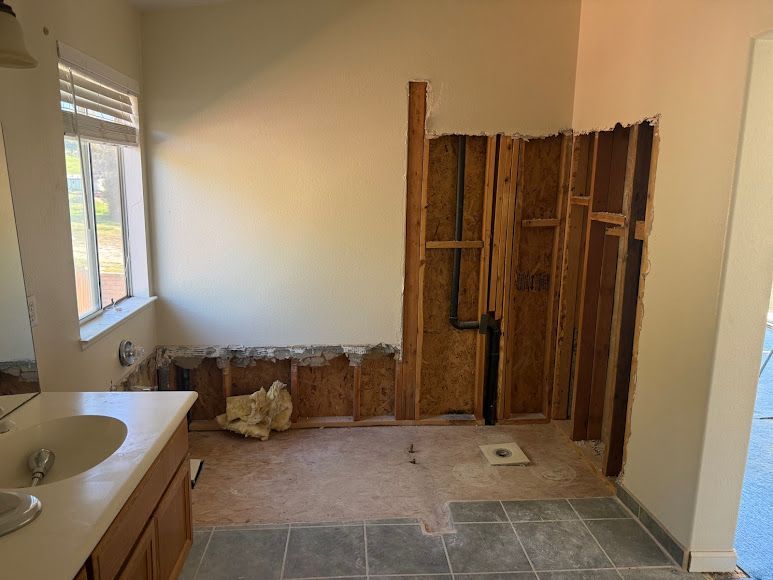Damaged bathroom with exposed wall studs, debris on the floor, and a sink under a window