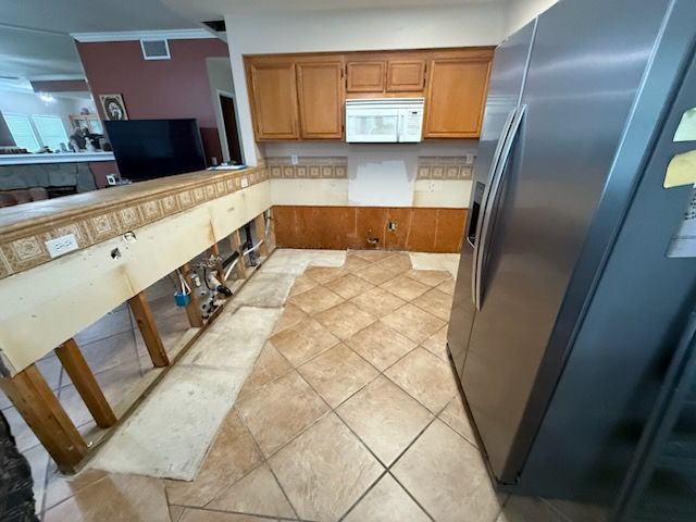 Kitchen under renovation with exposed sink area, tiled floor, wood cabinets, and a stainless steel refrigerator